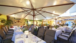 An outdoor dining area with tables set for two, covered by large umbrellas, and surrounded by chairs. - Hotel Hanauerhof (Appenweier)