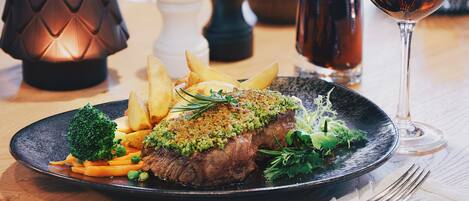 A plate of steak with vegetables and a glass of wine on a wooden table.