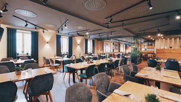 En moderne restaurant med flere spiseborde, stole og pendellamper.