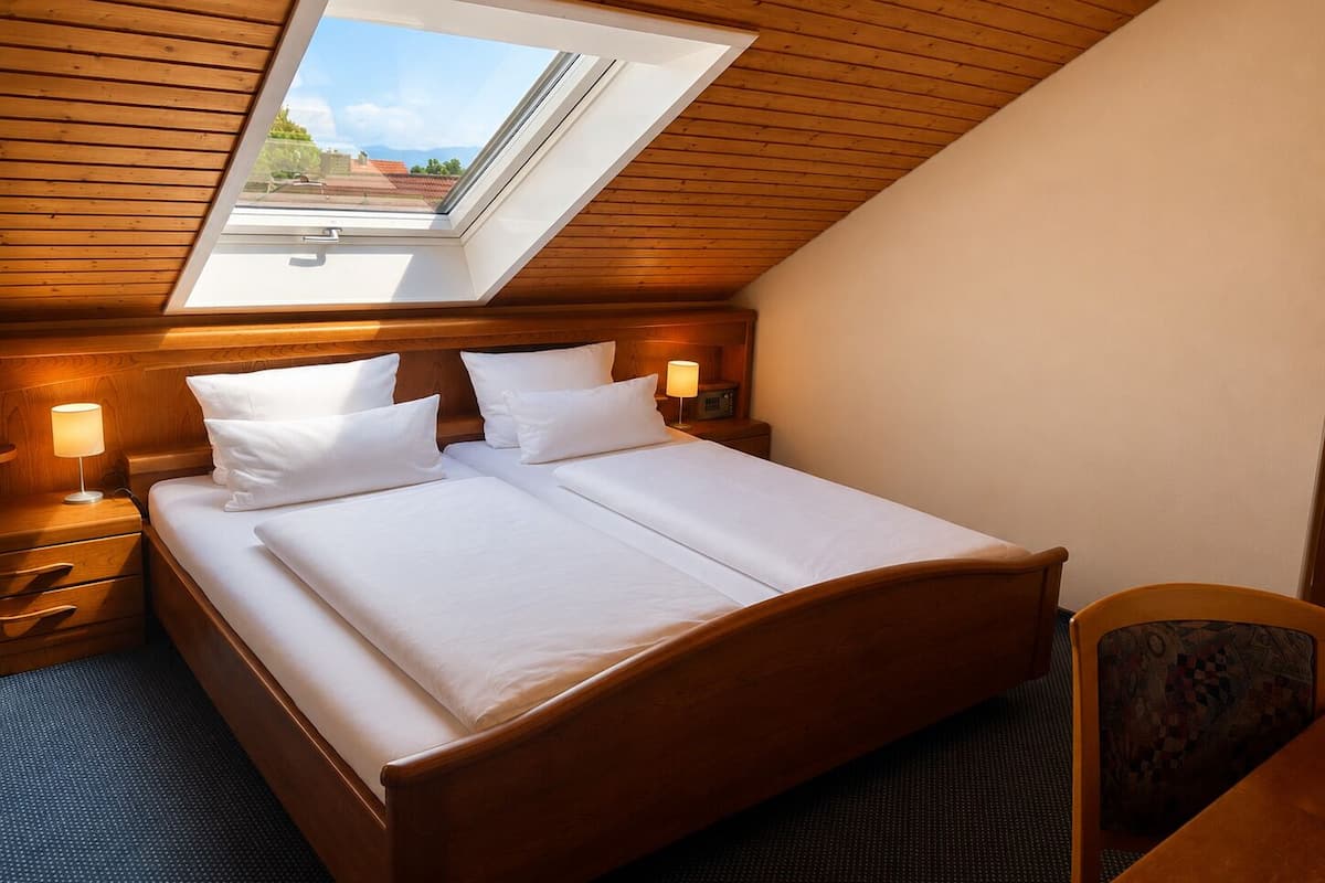 A bedroom with a skylight, wooden headboard, two bedside tables with lamps, and a chair.