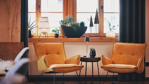 A room with two yellow chairs, a wooden floor, a window with curtains, a small table with a plant, and a potted plant on the windowsill. - Hotel Hanauerhof (Appenweier)