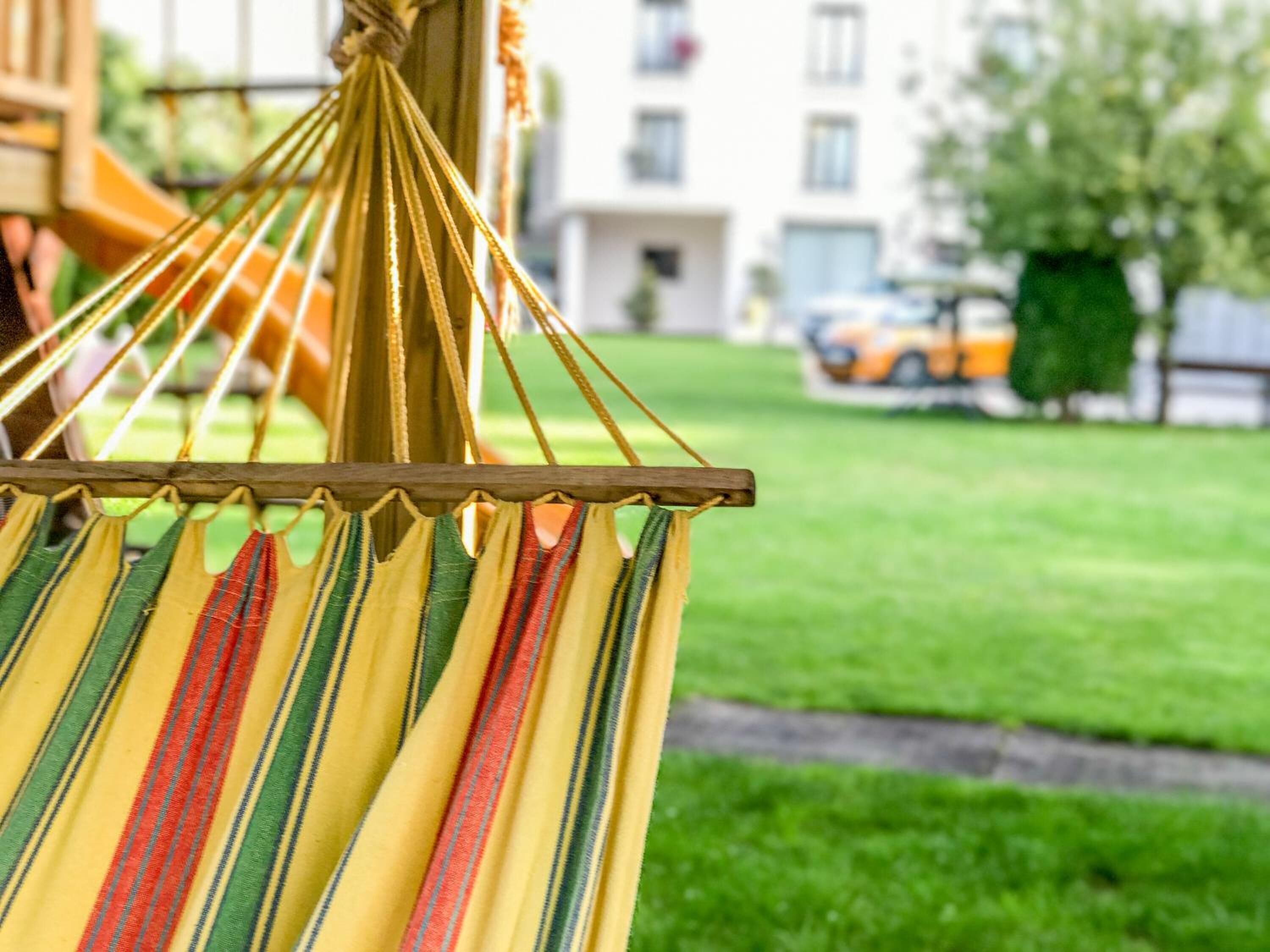 A hammock with multicolored stripes, suspended outdoors with a grassy lawn and a building in the background.