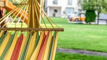 A hammock with multicolored stripes, suspended outdoors with a grassy lawn and a building in the background.