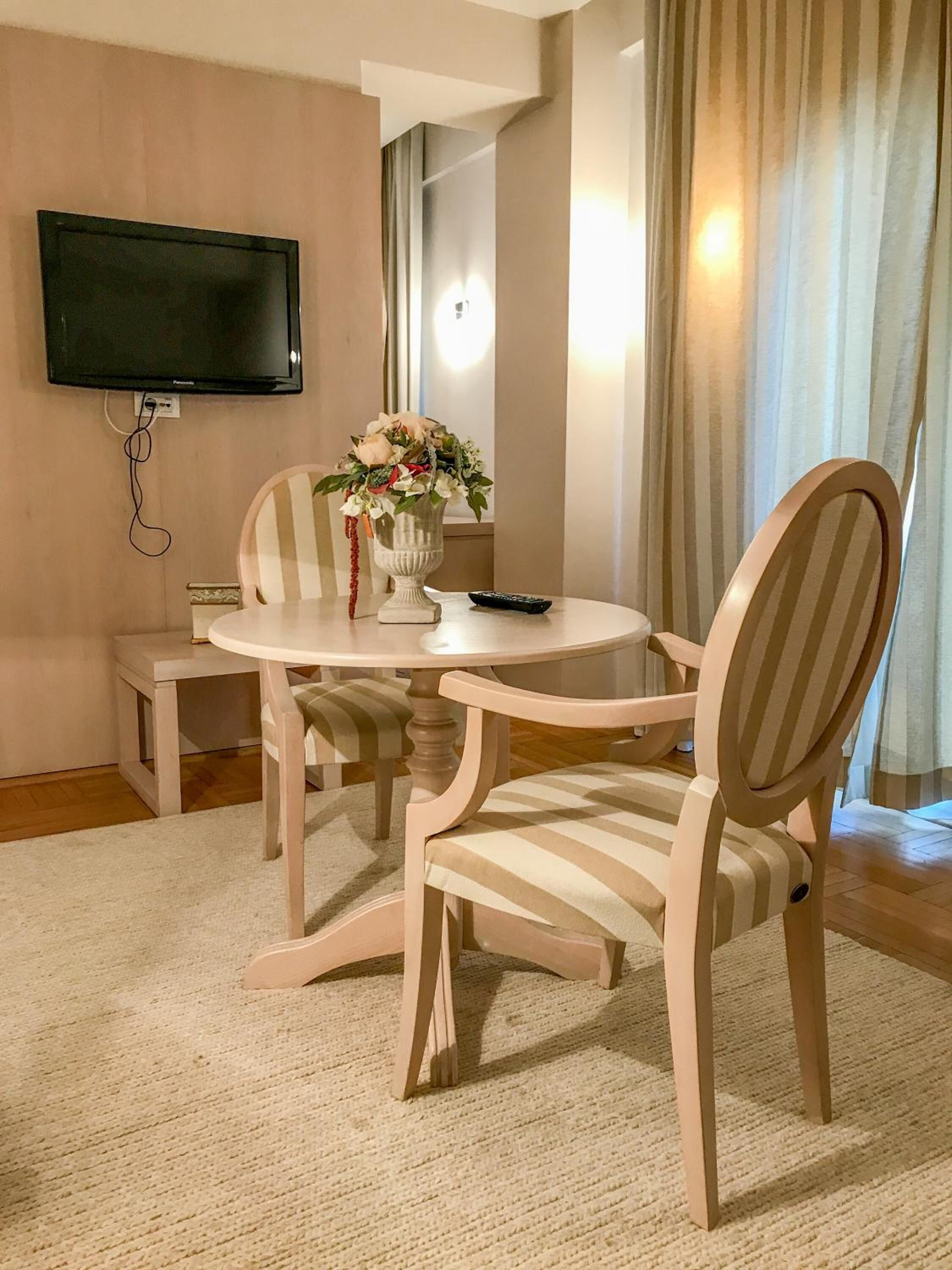 Un comedor con una mesa redonda, sillas a rayas, un florero con flores, un control remoto y un televisor de pantalla plana montado en la pared.