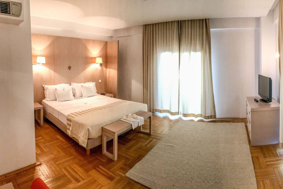 A hotel room with a large bed, bedside tables, a TV, and a window with curtains.