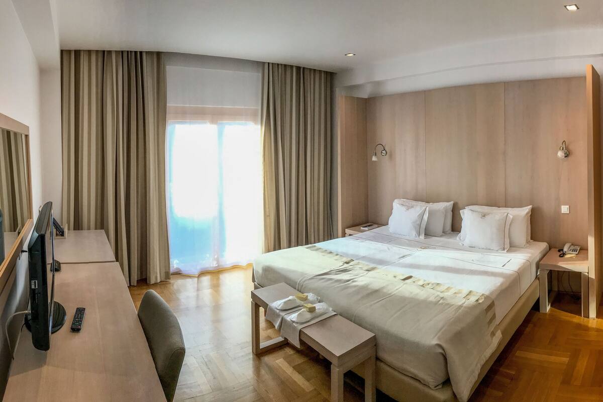 A hotel room with a large bed, a desk with a chair, a television, and a desk lamp.