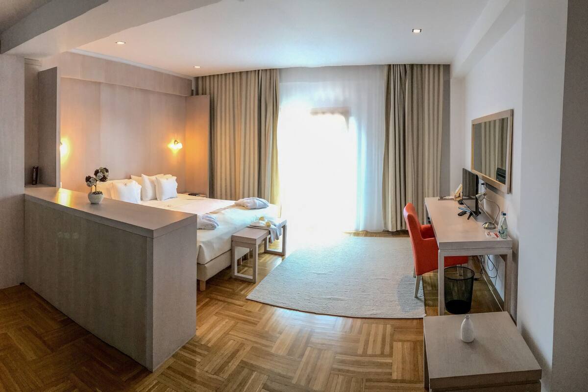 A hotel room with a bed, a desk, a chair, a small table, and a bathroom area.