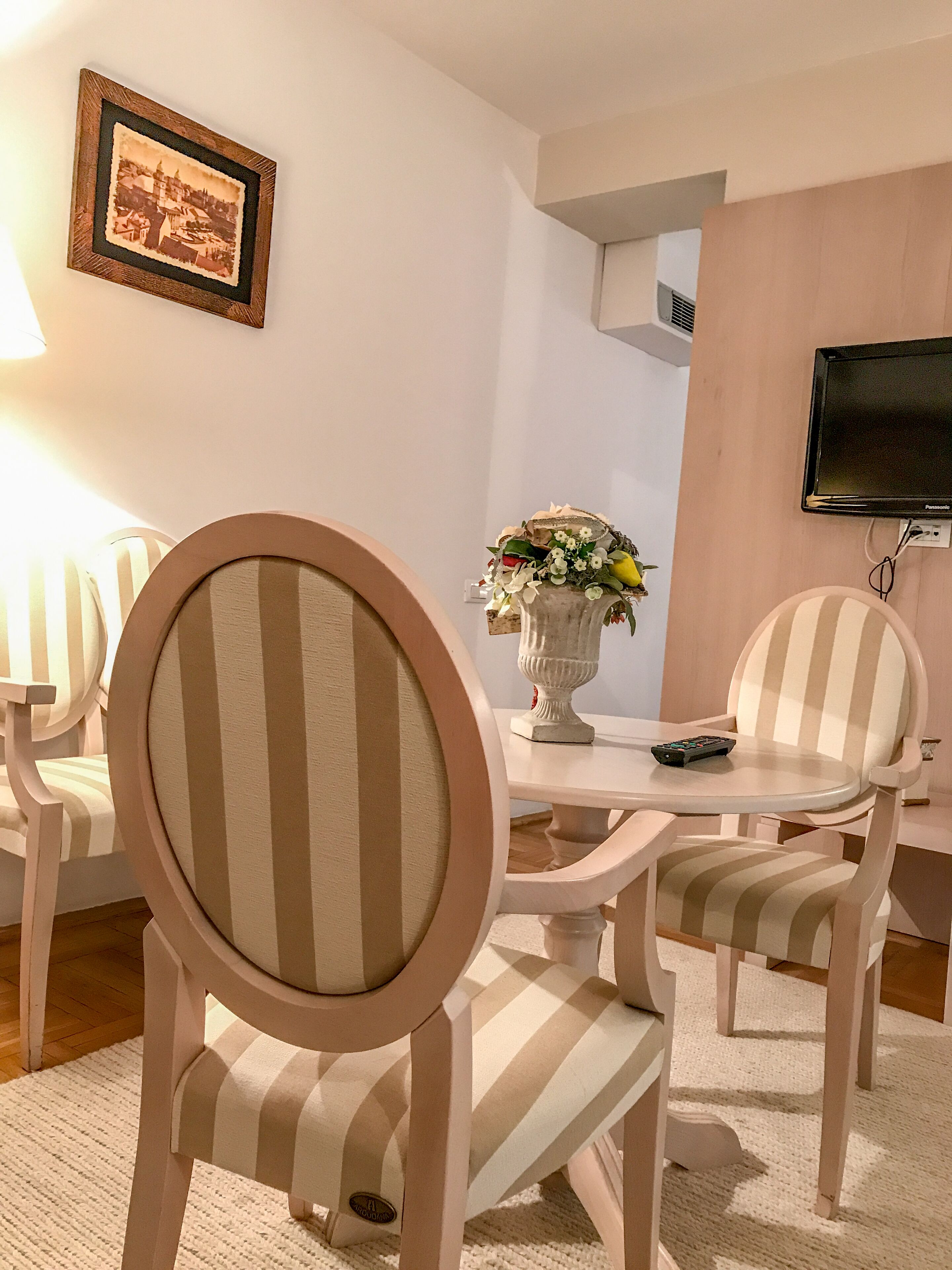 Un coin repas avec des chaises à rayures, une table ornée d’un vase de fleurs et un téléviseur fixé au mur.