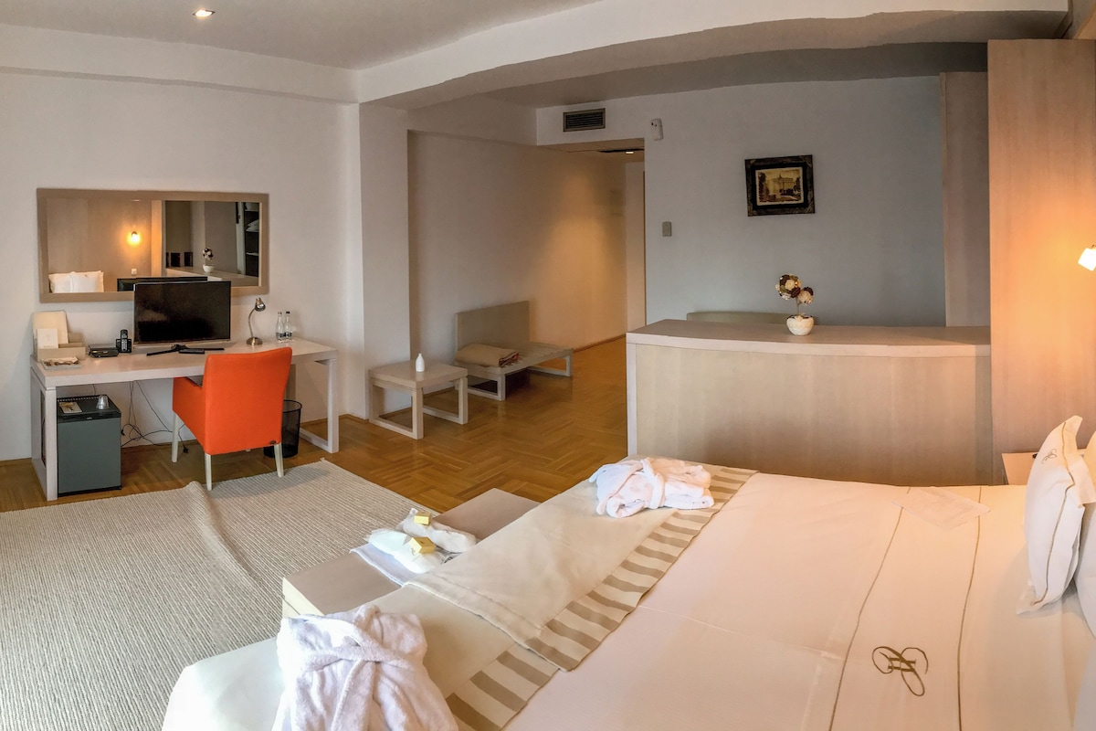 A hotel room with a bed, a desk, a chair, a small table, and a TV.