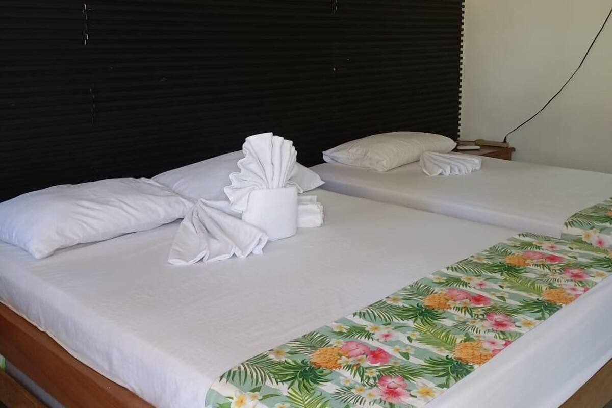 Una cama doble con sábanas blancas, cabecera de madera y colcha estampada.