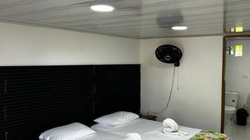 A hotel room with a large bed, a wooden headboard, a black ceiling fan, and a bathroom visible through an open door.