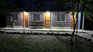 Una pequeña casa de ladrillo con puerta de madera, banco y plantas en macetas.