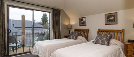 A bedroom with two beds, a balcony, and a view of a house.