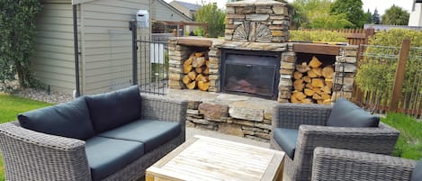 An outdoor patio area with wicker furniture, a stone fireplace, and a fire pit.