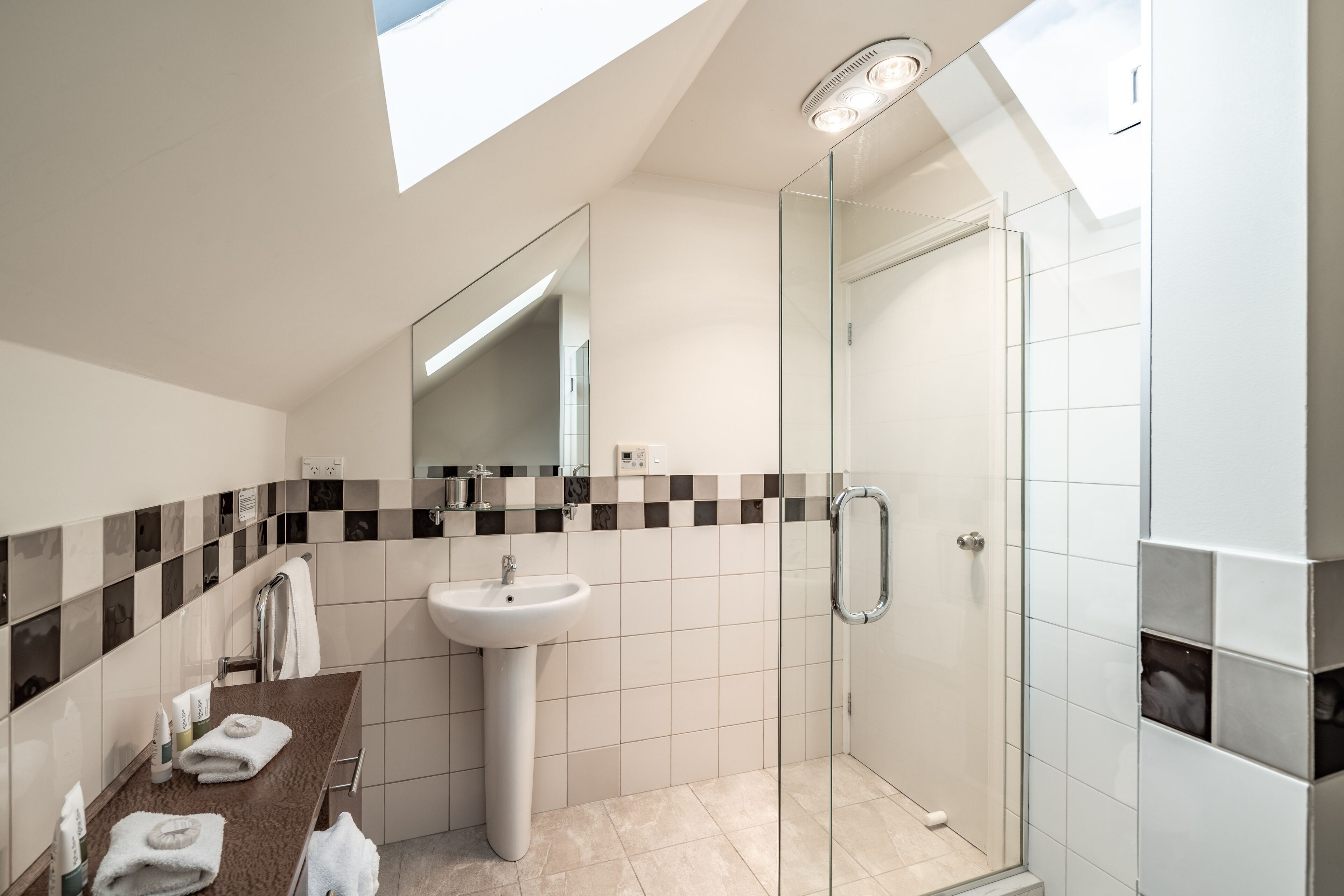 A modern bathroom with a skylight, a glass shower enclosure, and a vanity with a sink and towel rack.