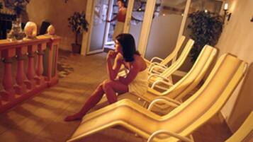A room with multiple sun loungers arranged in a row, a small table with decorative items, and a potted plant.