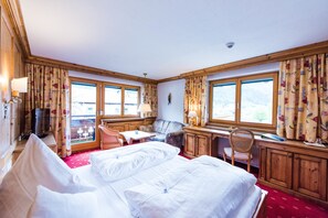 Habitación de hotel con una cama grande, un escritorio, una silla y vistas a las montañas a través de las ventanas.