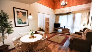 A living room with a wooden ceiling, a dining table with chairs, a sofa, a TV on a stand, and a potted plant. - Hotel Petit Casa da Montanha (Gramado)