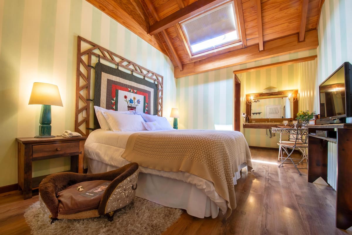 A bedroom with a bed, bedside tables, a desk, a chair, a small sofa, and a window.