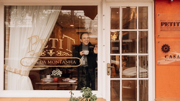 A hotel entrance with a sign reading "PETIT CASA DA MONTANHA" and a person standing at the door. - Hotel Petit Casa da Montanha (Gramado)