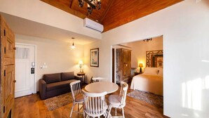 A cozy room with a wooden ceiling, a round dining table with chairs, a sofa, and a bed with a nightstand. - Hotel Petit Casa da Montanha (Gramado)
