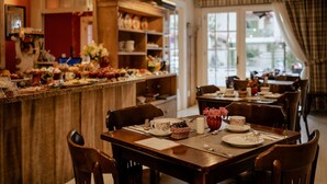 A restaurant with wooden tables and chairs, a bar area with various food items, and a view of the outdoors through large windows. - Hotel Petit Casa da Montanha (Gramado)