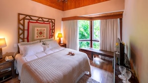 A neatly arranged bedroom with a large bed, bedside lamps, a wooden bench, and a window with curtains. - Hotel Petit Casa da Montanha (Gramado)
