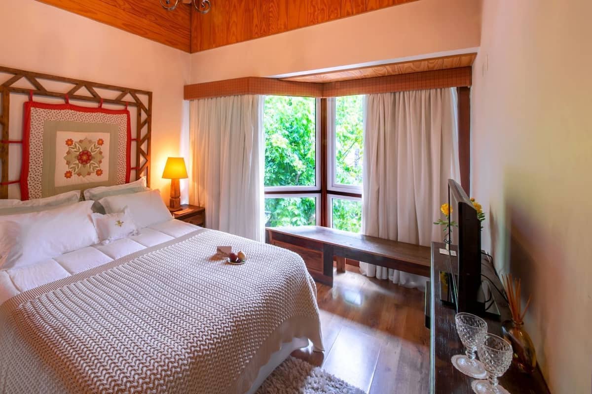 A neatly arranged bedroom with a large bed, bedside lamps, a wooden bench, and a window with curtains.