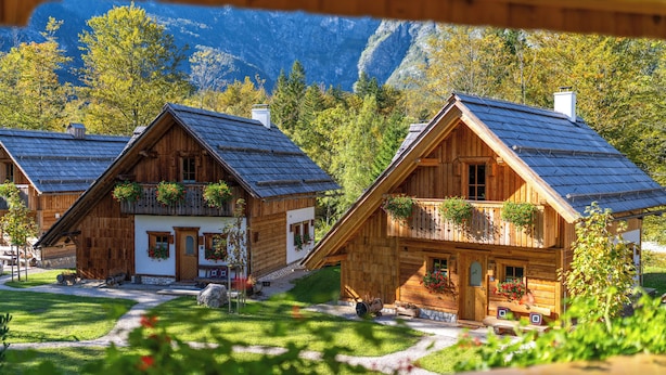 A wooden cabin with a balcony, surrounded by a well-maintained garden and a mountainous backdrop. - ALPIK Chalets - Bohinj (Bohinj)