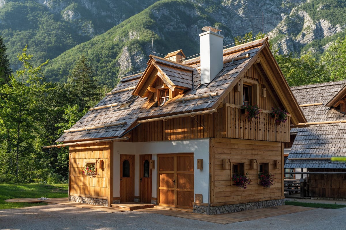 A wooden chalet with a sloped roof, stone foundation, and wooden doors.