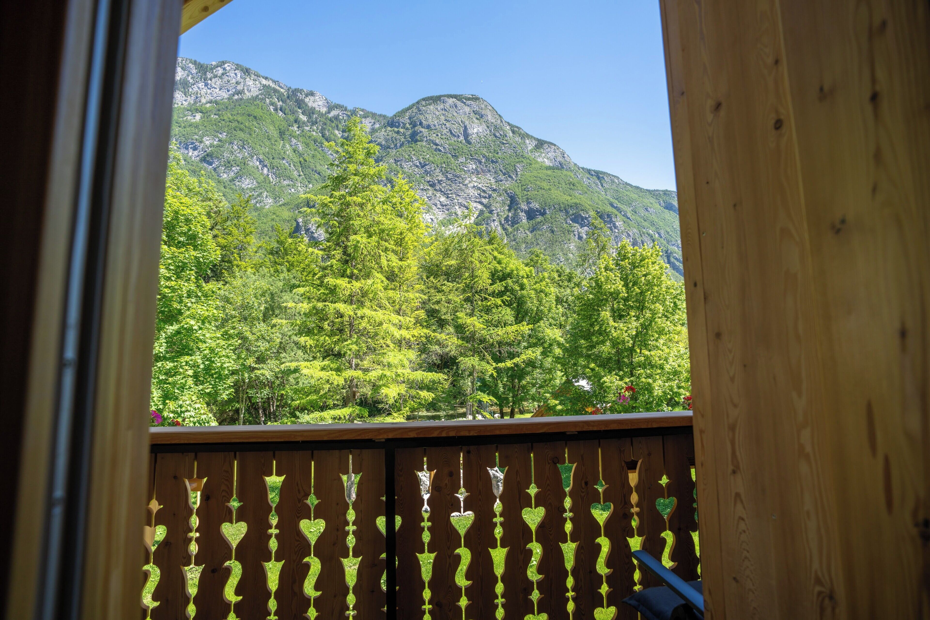 A wooden balcony with heart-shaped cutouts, overlooking a forested mountain.