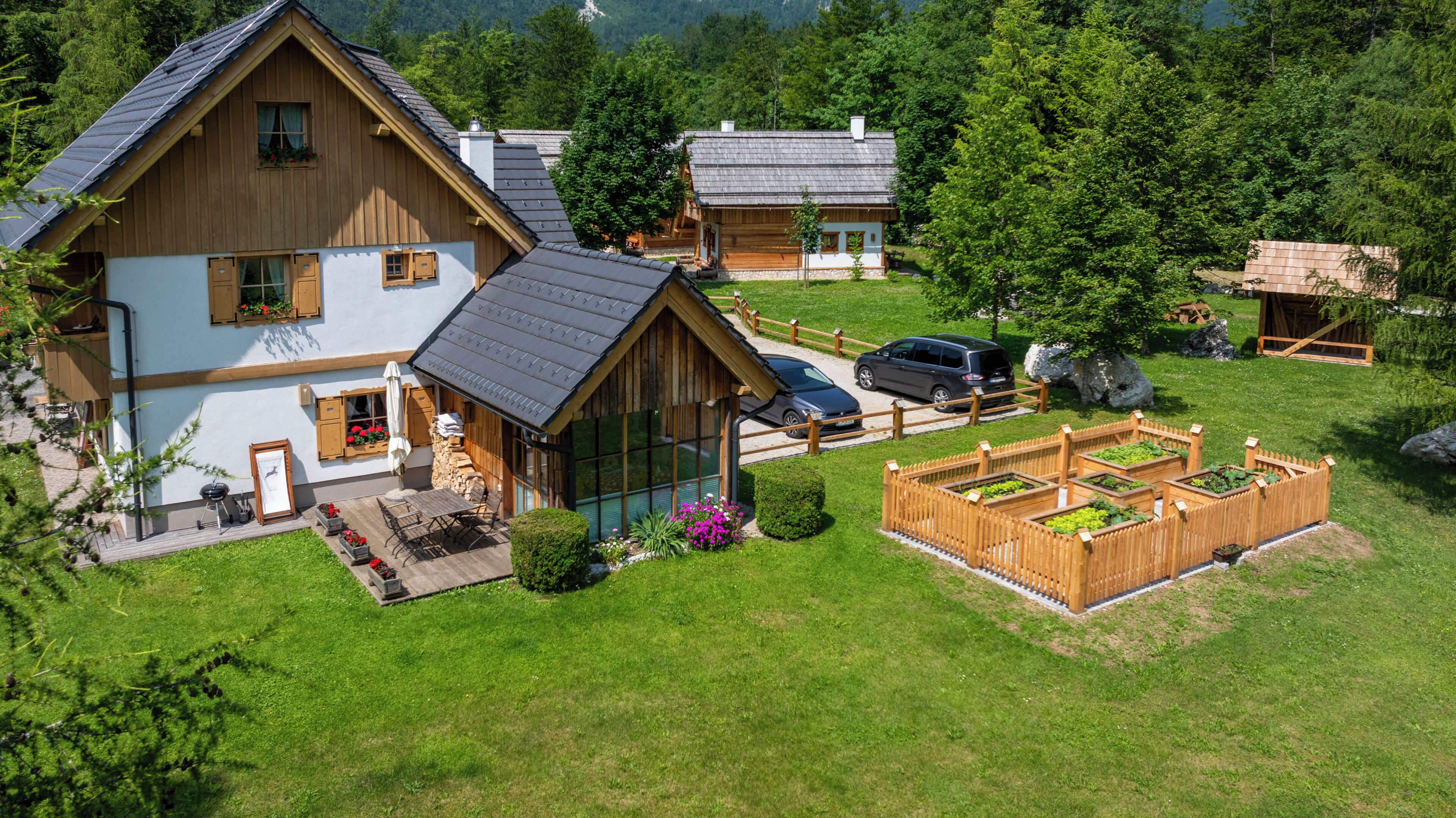 A wooden house with a sloped roof, a patio with outdoor furniture, and a vegetable garden.