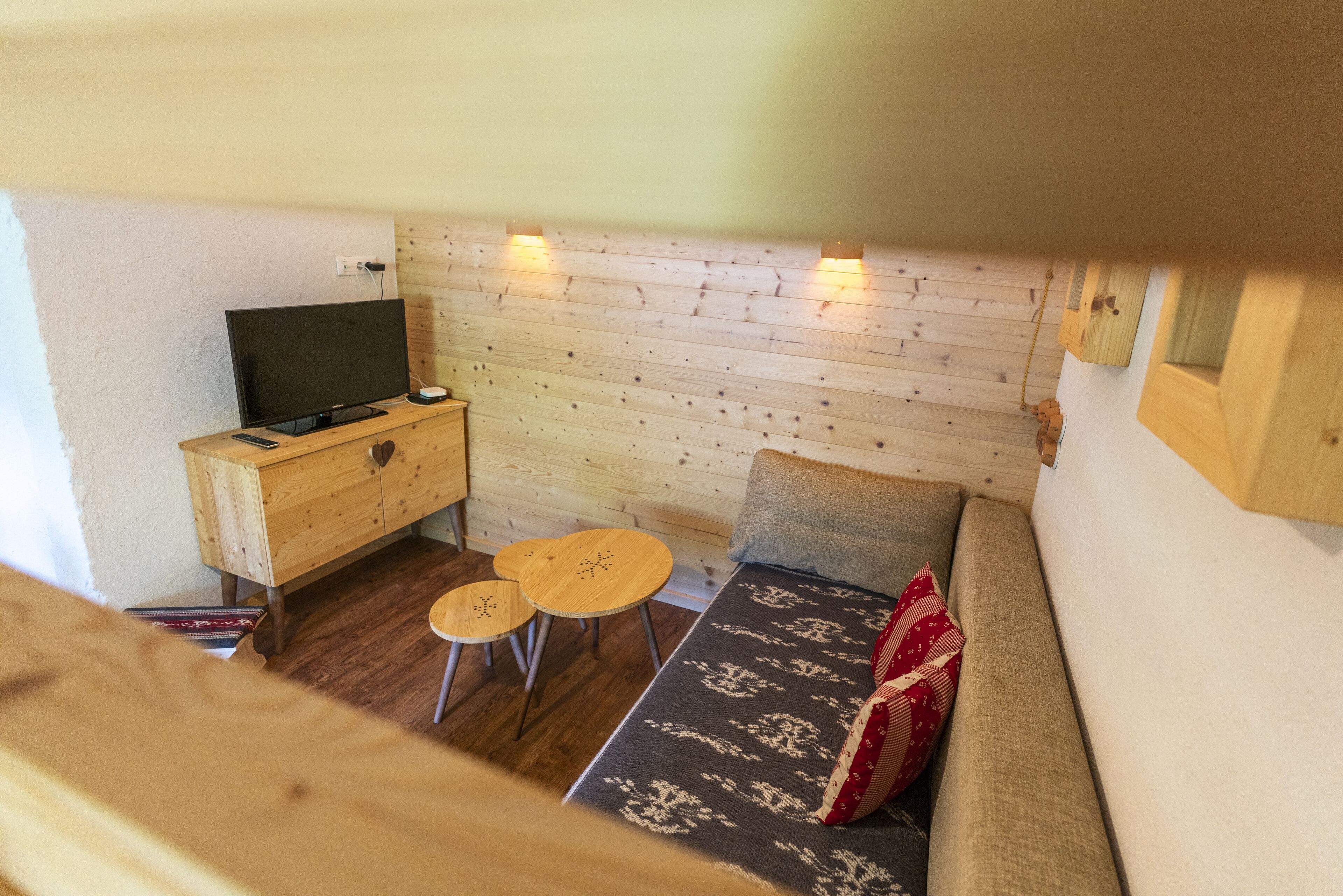 A cozy room with a wooden wall, a sofa, a TV on a wooden cabinet, and two small round tables.
