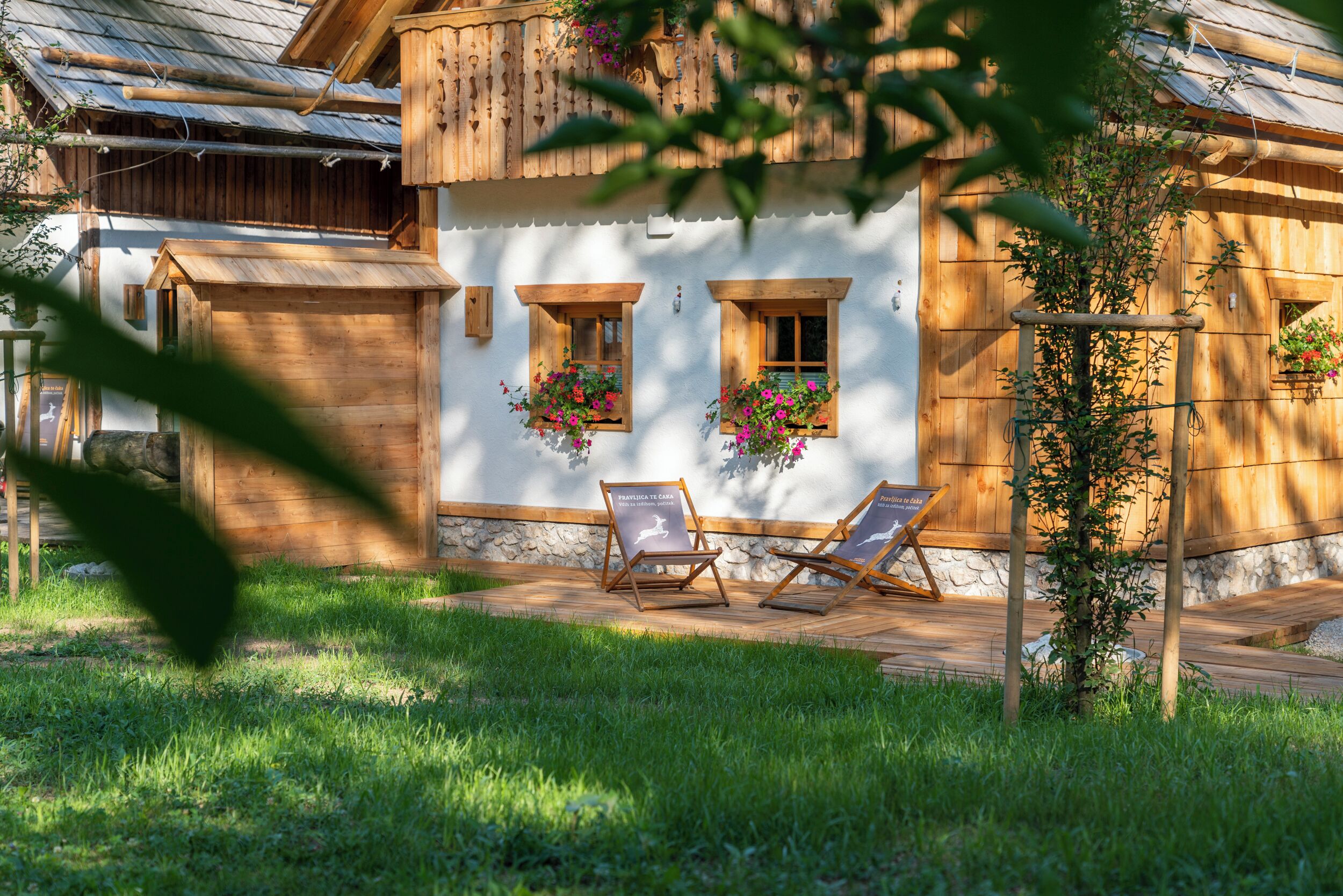 A wooden house with two windows, a small porch, and two lounge chairs.