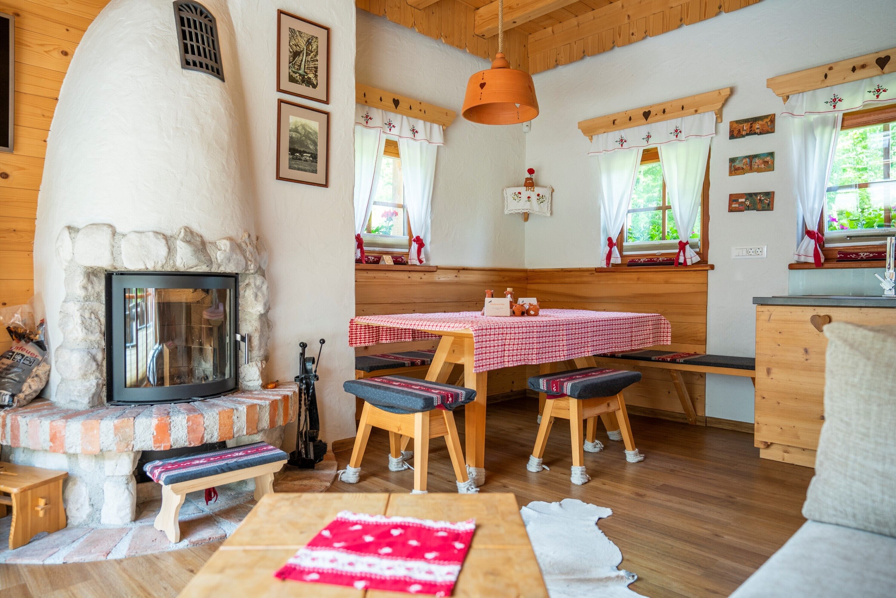 Ein gemütliches Zimmer mit Kamin aus Stein, Holzmöbeln und einem Esstisch mit kariertem, rotem Tischläufer.
