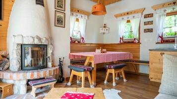 Ein gemütliches Zimmer mit Kamin aus Stein, Holzmöbeln und einem Esstisch mit kariertem, rotem Tischläufer.