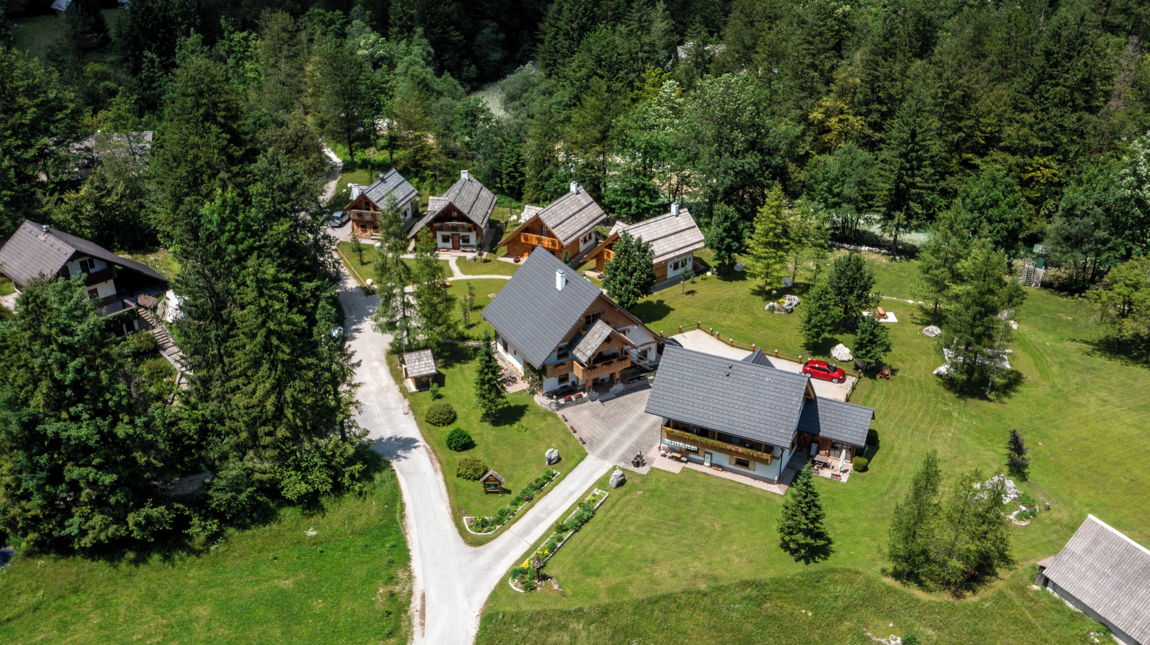 An aerial view of a residential area with multiple houses, a central road, and surrounding greenery.