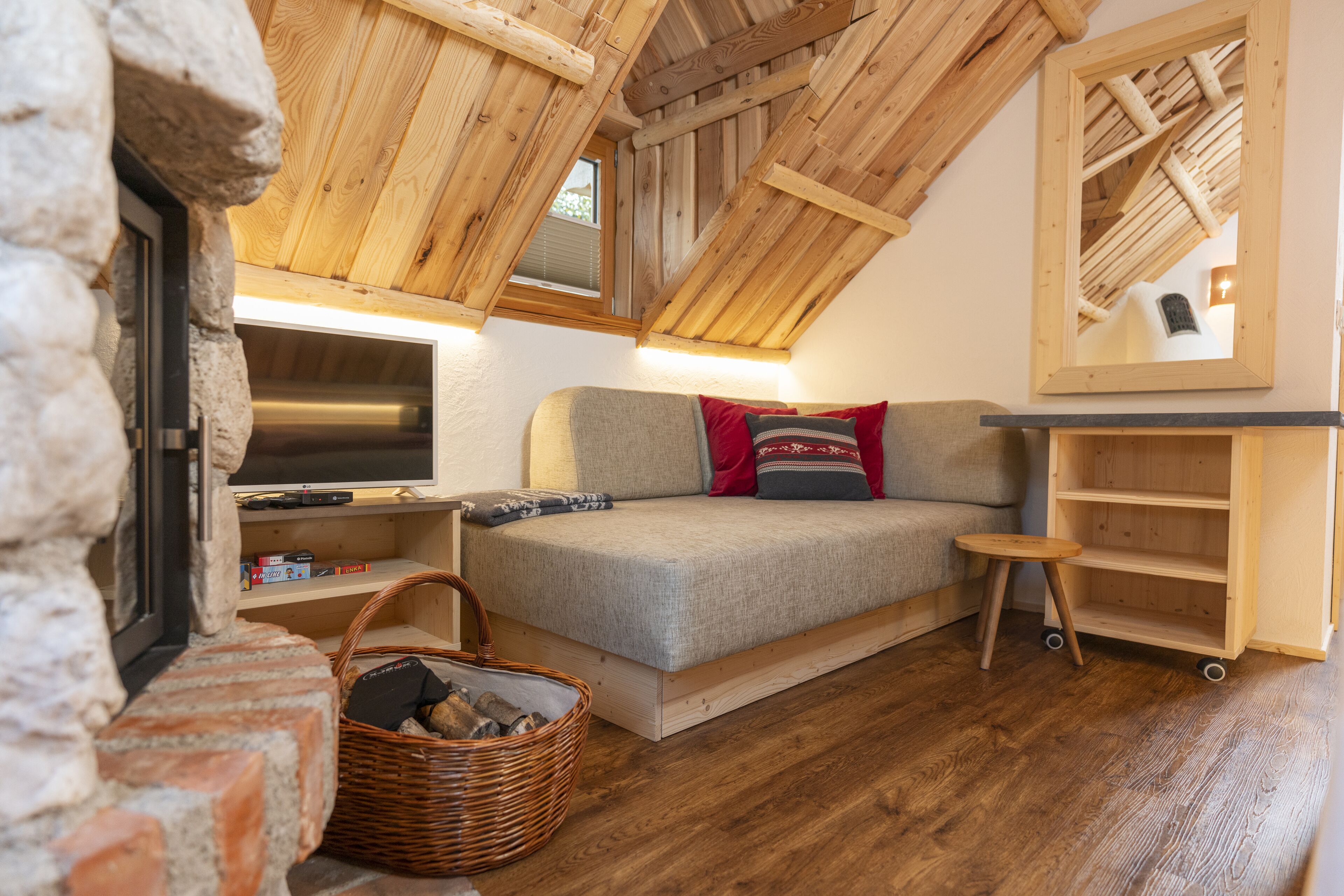 Un dormitorio estilo loft acogedor, con techo de madera, sofá cama, televisor, una mesita pequeña y una cesta de mimbre.