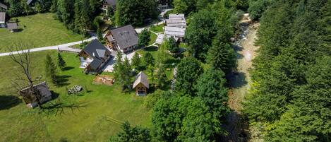An aerial view of a residential area with multiple houses, a central building with a large porch, and a winding path through the trees.