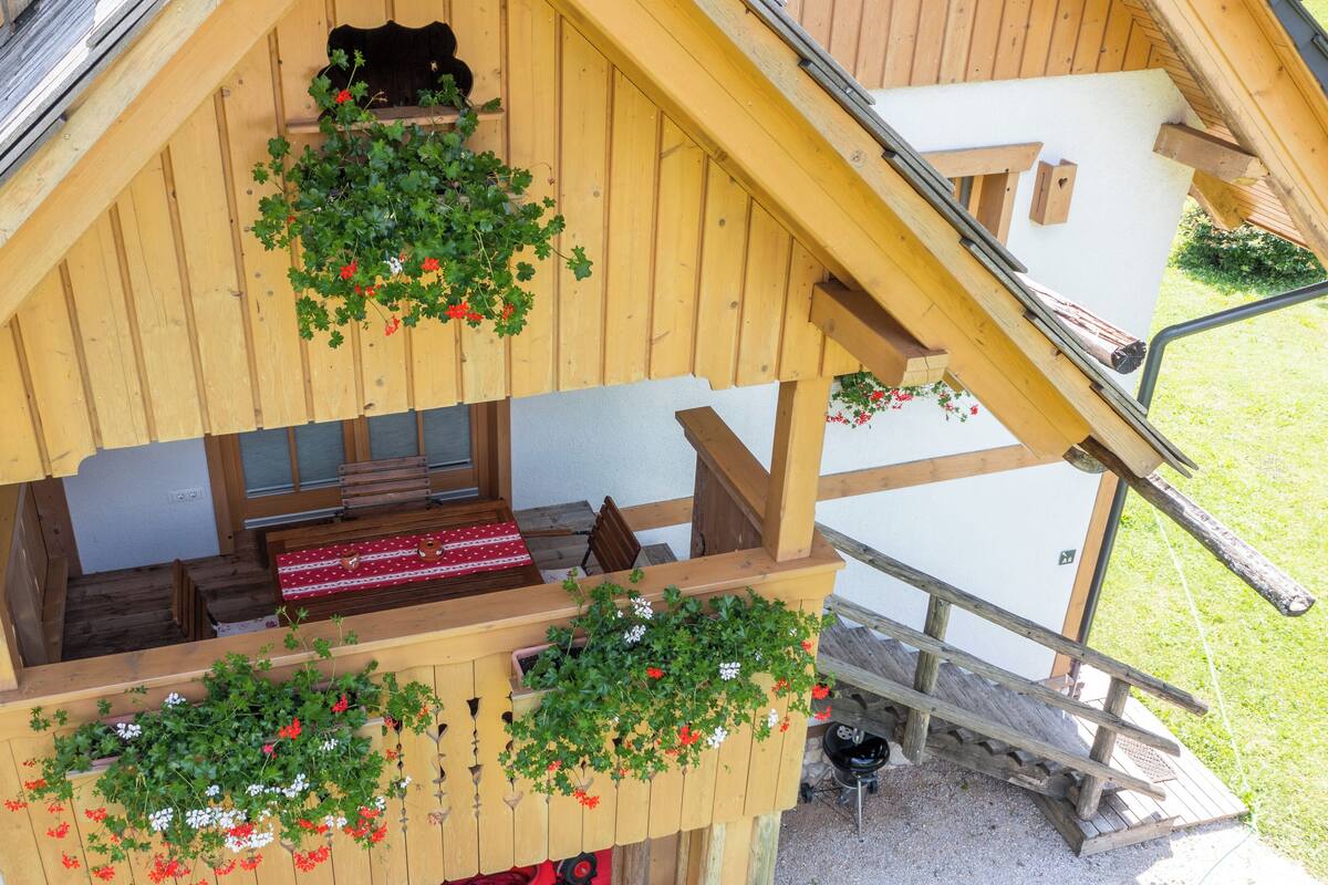 A wooden chalet with a balcony, a wooden bench, and hanging flower baskets.