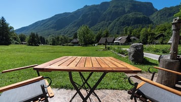 A wooden table and chairs on a stone patio with a view of a mountain and houses in the background.