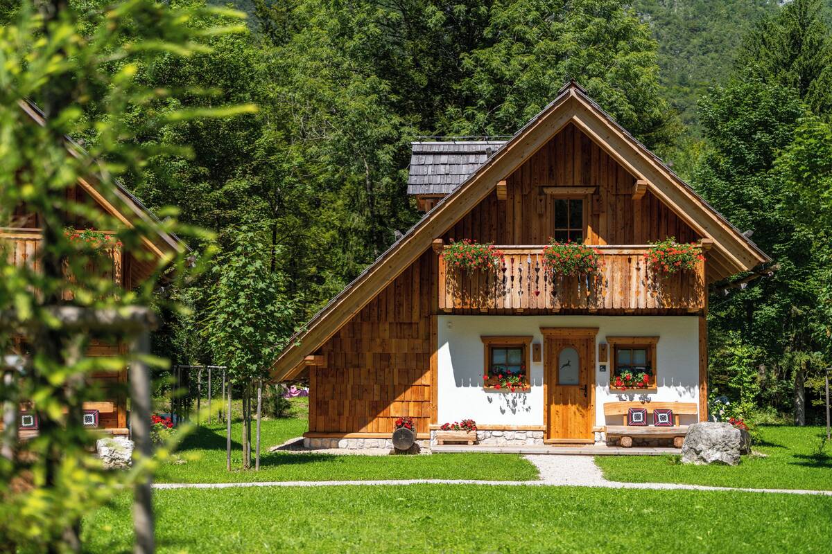 A wooden chalet with a balcony, a stone foundation, and a white exterior.