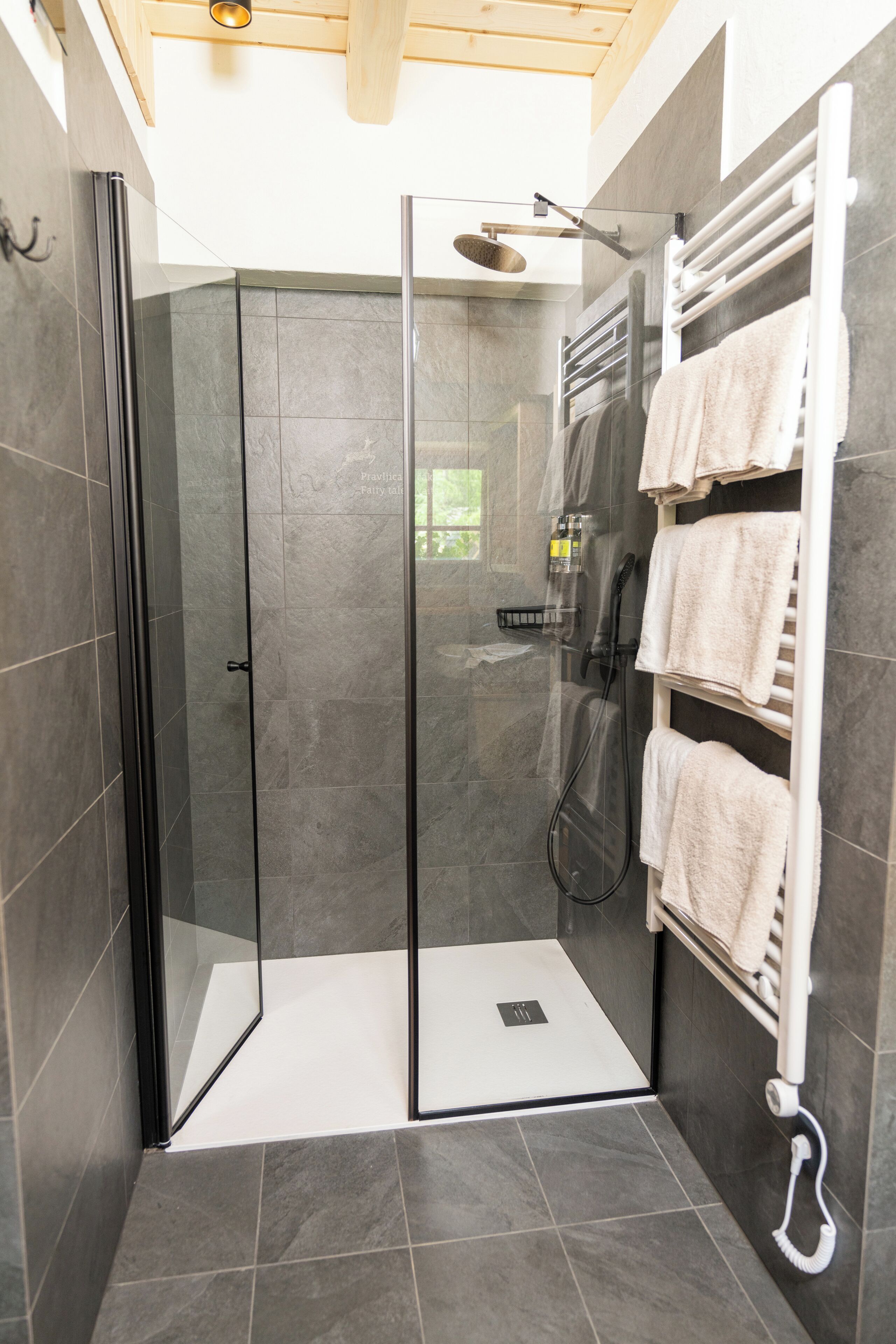 Ein modernes Badezimmer mit Glasduschtür, Handtuchhalter und mehreren Handtüchern sowie einer Duschbrause.