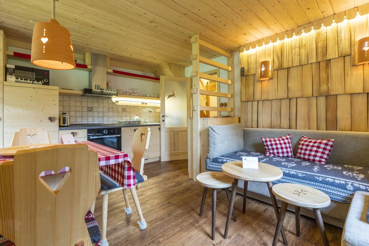 A cozy, wooden-furnished room with a dining area, a sofa with patterned cushions, and a kitchen area with modern appliances.