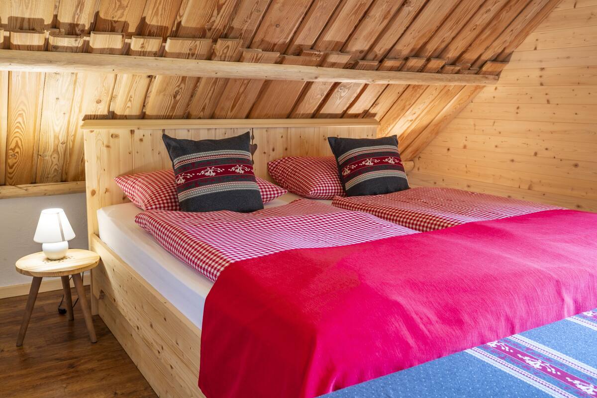 A wooden cabin bedroom with a bed, pillows, a lamp, and a small table.