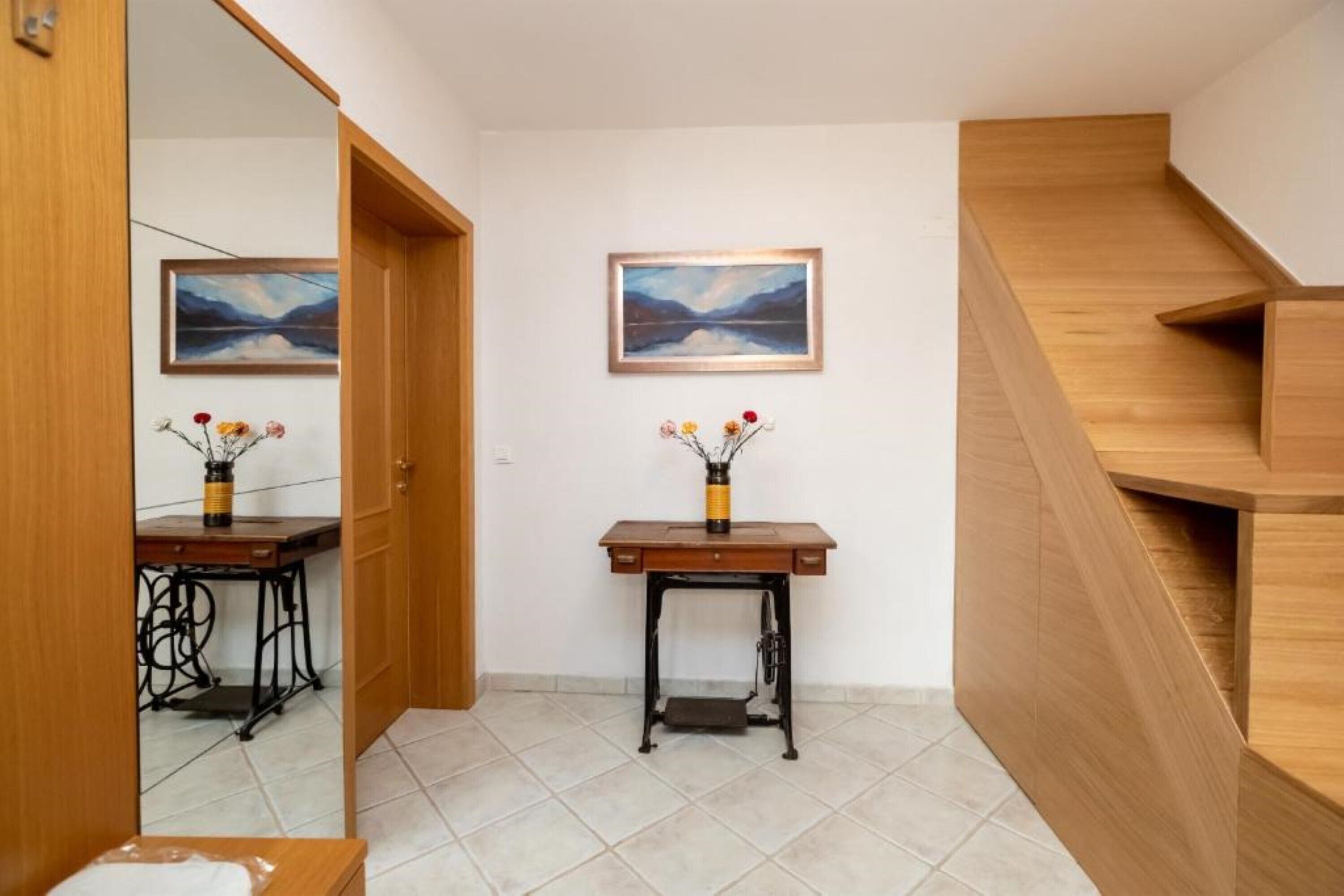 Un pasillo con una escalera de madera, dos cuadros en la pared y una pequeña mesa con un florero.