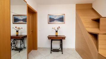 Un pasillo con una escalera de madera, dos cuadros en la pared y una pequeña mesa con un florero.