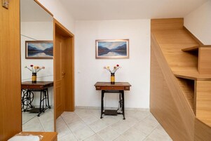Un pasillo con una escalera de madera, dos cuadros en la pared y una pequeña mesa con un florero.