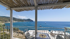 A terrace with a view of the sea, featuring a table and chairs, and a thatched roof structure. - Hotel La Palma (Serrara Fontana)