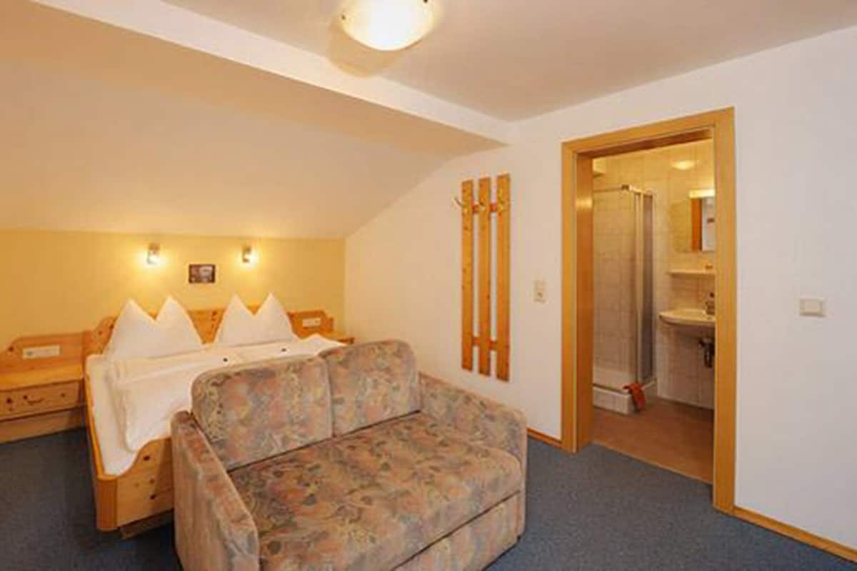 Une chambre à coucher avec un lit, un canapé, une tête de lit en bois et une salle de bain visible à travers une porte ouverte.